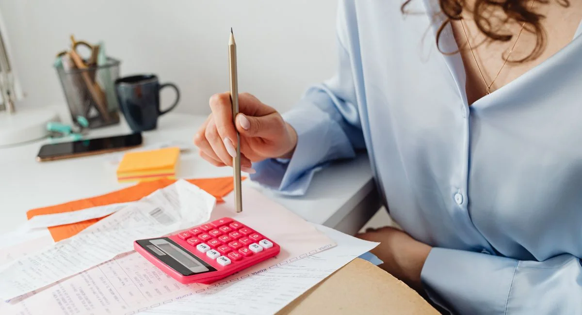 A woman is calculating expenses using a calculator and papers at her desk.
