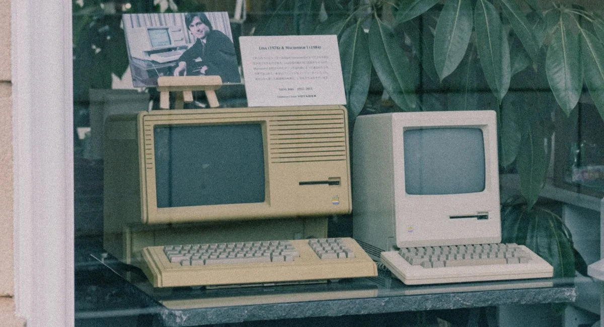 Retro Apple computers with keyboards displayed in a Tokyo store window, showcasing early tech design.