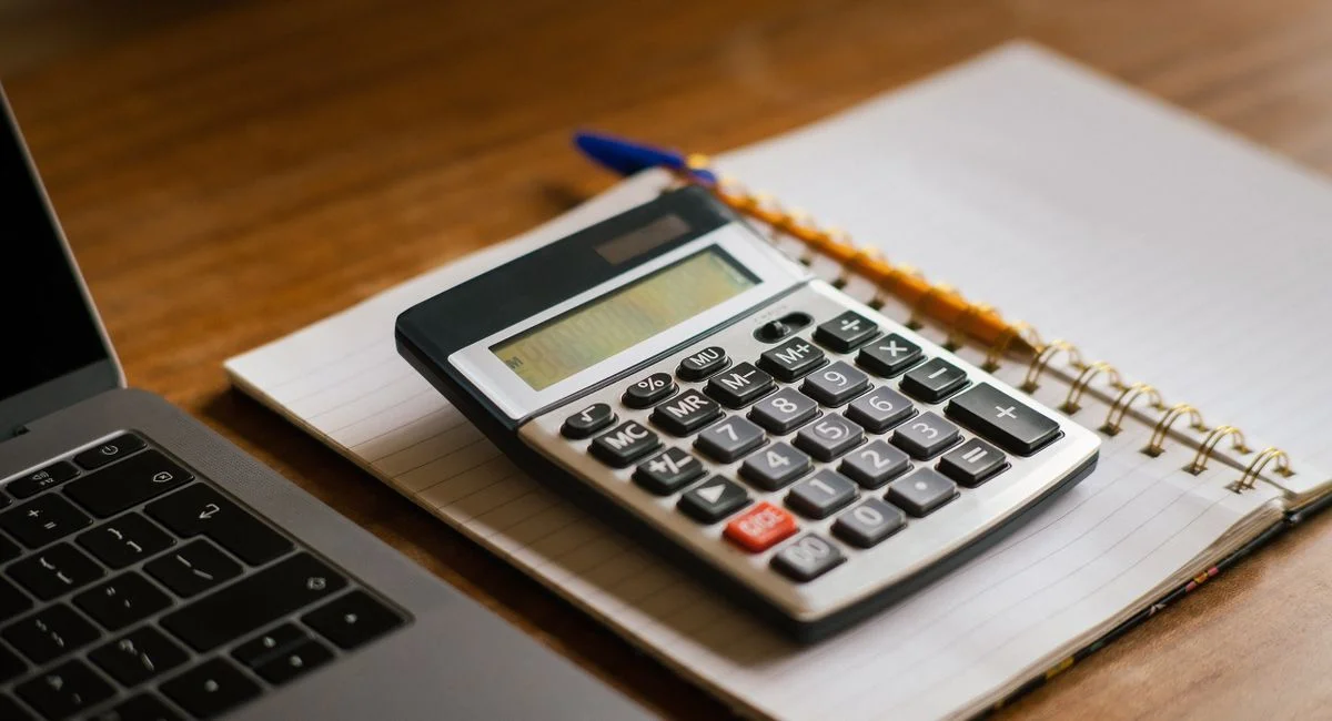 Calculator and open laptop on wooden desk, ideal for financial or accounting tasks.