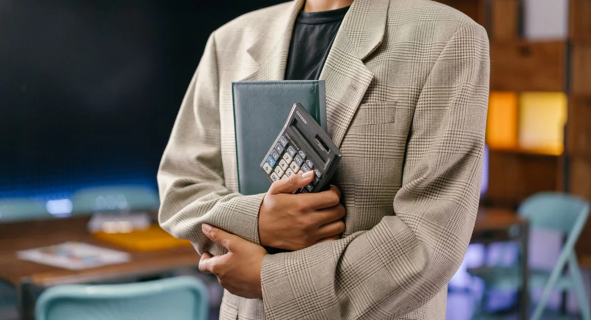 A young professional holds a calculator and notebook in an office setting.