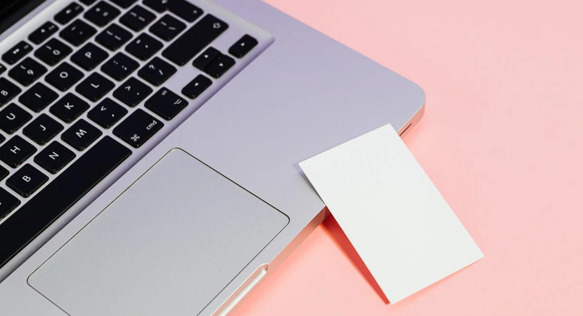 Close-up of a laptop with a blank card on a pink background, ideal for tech concepts.