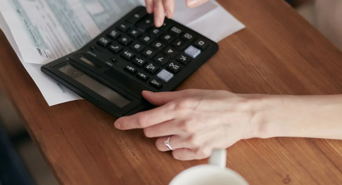 A woman uses a calculator to manage finances at home, focused on budget planning.