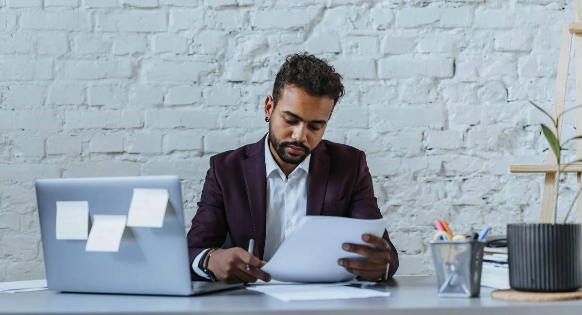 A professional man reviews documents in a modern office setting, focused on his work.