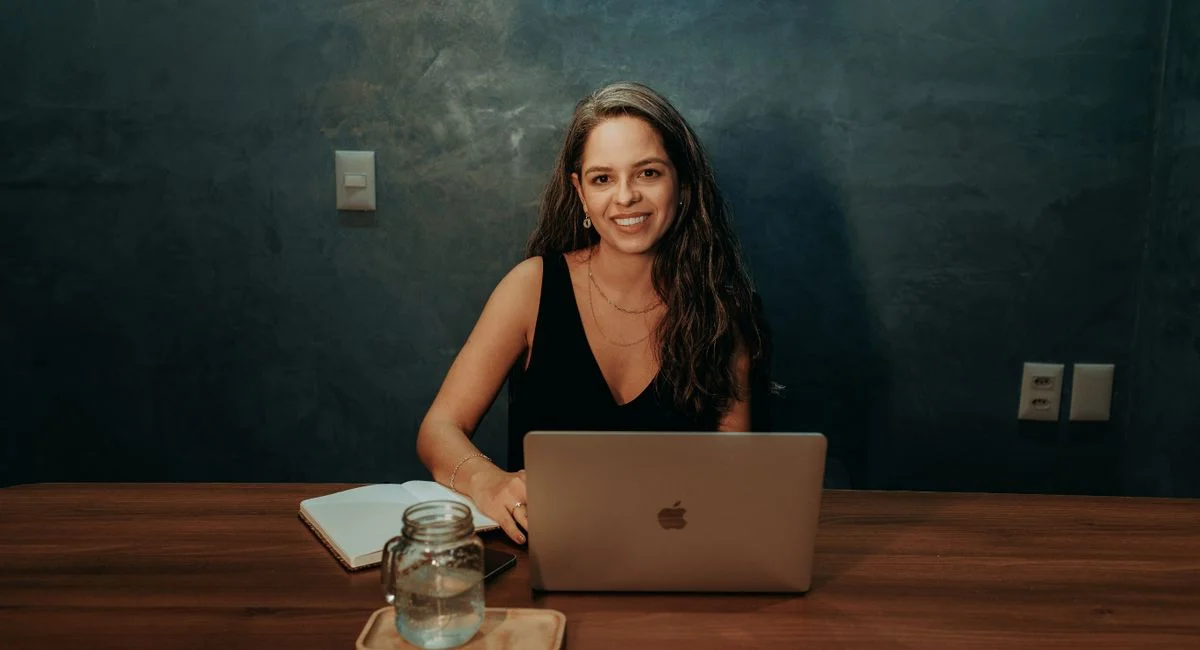 Woman working on a laptop in a cozy home office, smiling at the camera.
