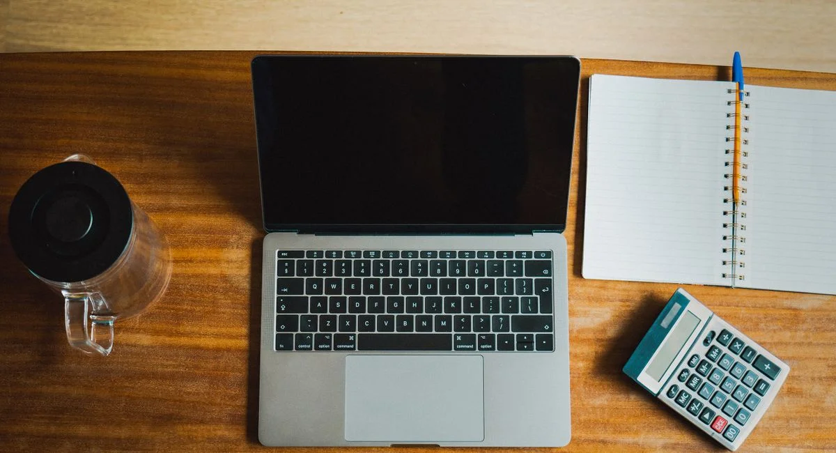 Flat lay of workspace featuring a laptop, calculator, and notebook on a wooden desk.