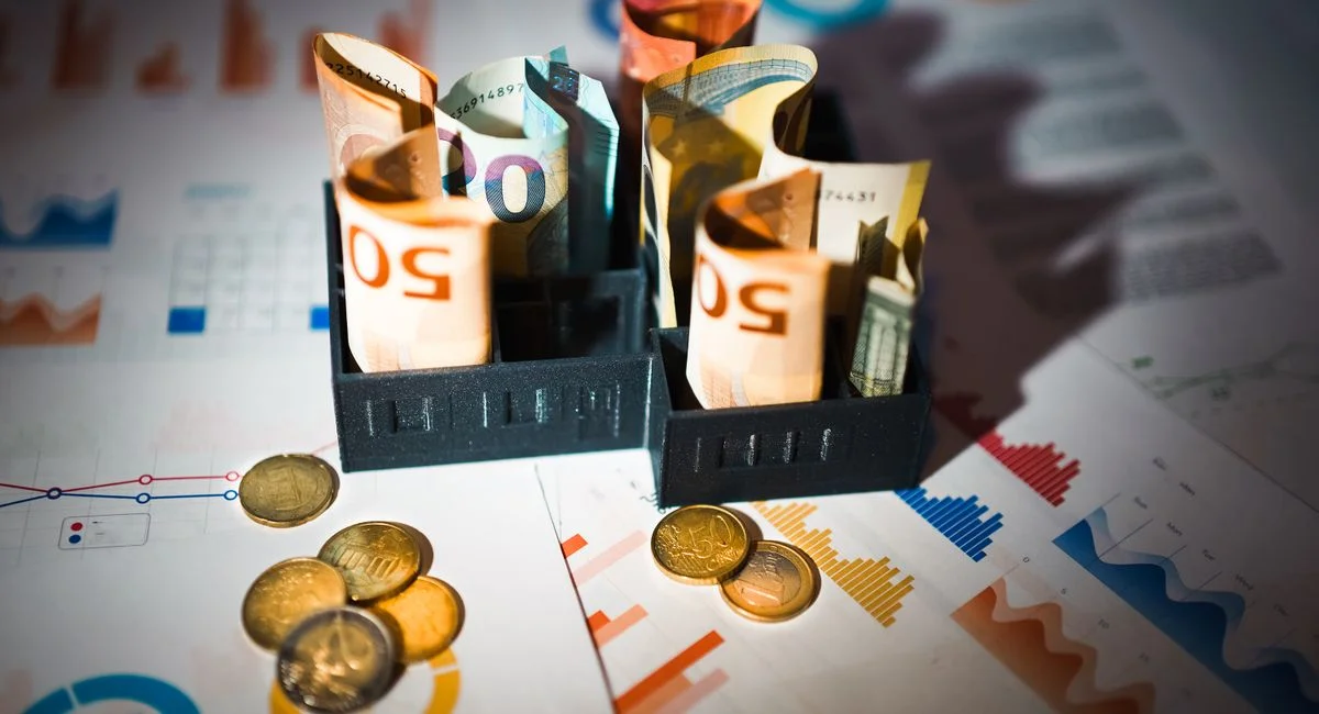 A close-up of euro banknotes and coins on top of financial charts symbolizing investment and economic analysis.