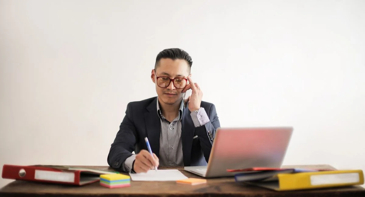 Focused businessman multitasking at desk, engaged in a phone call and working on a laptop.