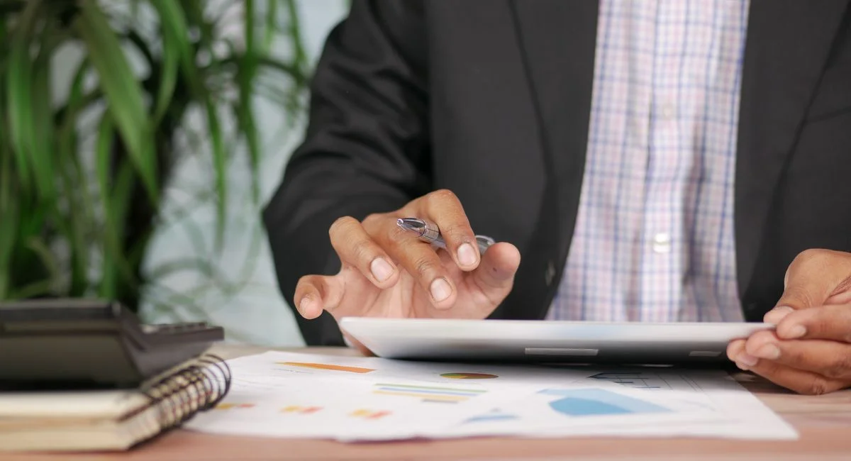Business professional in suit using tablet with pen on desk with documents and calculator.