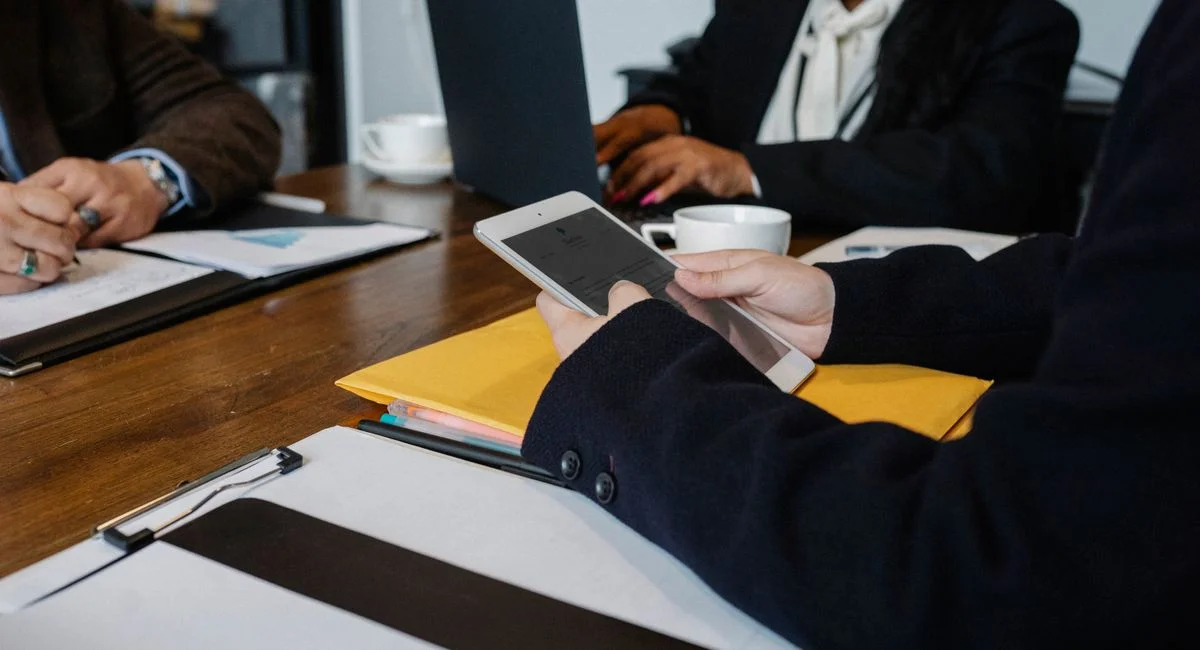 Crop faceless coworkers in formal wear gathering at table with gadgets and documents for brainstorm