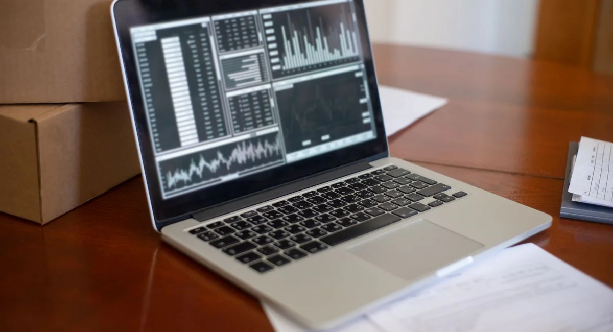Laptop showing data graphs on wooden table with cardboard boxes, depicting a small business office setting.