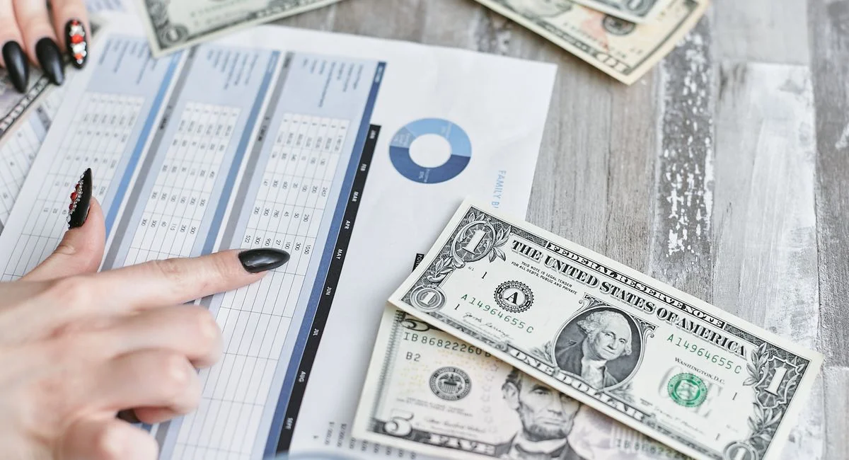 Close-up of hands analyzing financial document with US dollar bills on table.