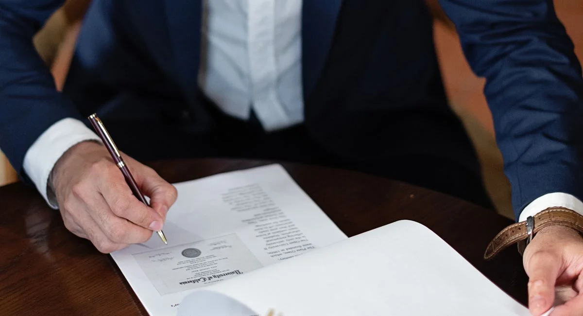 A professional individual signs legal documents at a desk in an office setting.
