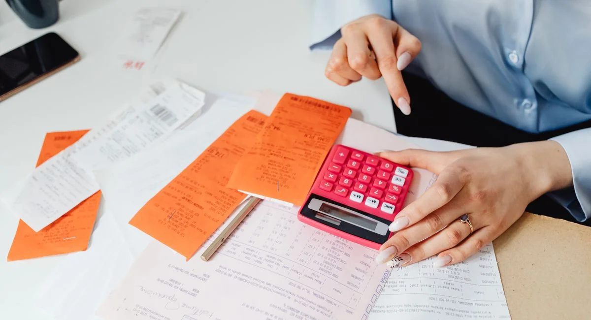 Businesswoman calculates expenses using receipts and calculator at desk. Ideal for finance, accounting themes.