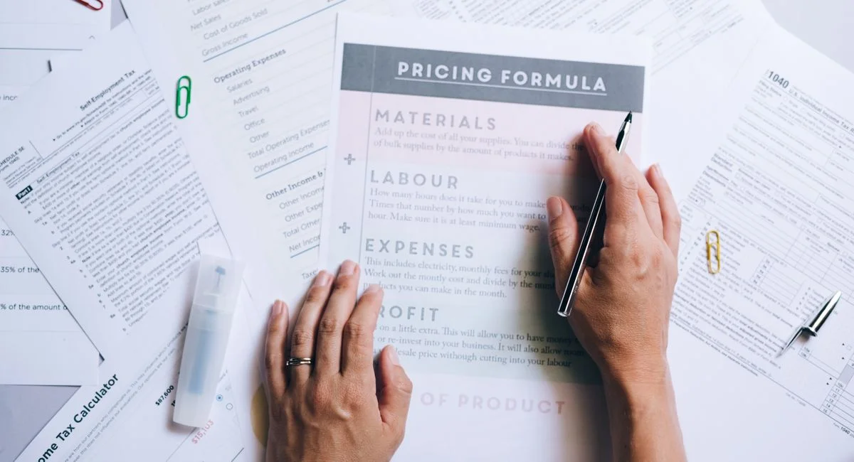 Hands organizing business documents and pricing formula papers on an office desk.