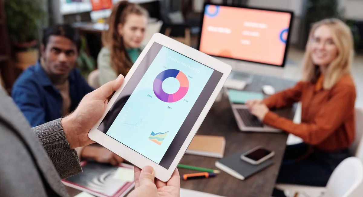 Business team using a tablet to analyze digital marketing data with charts in an office setting.