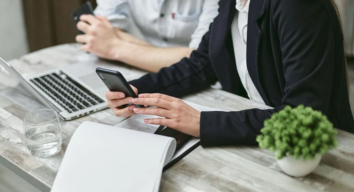 Two professionals collaborating in a business meeting using a smartphone and laptop.