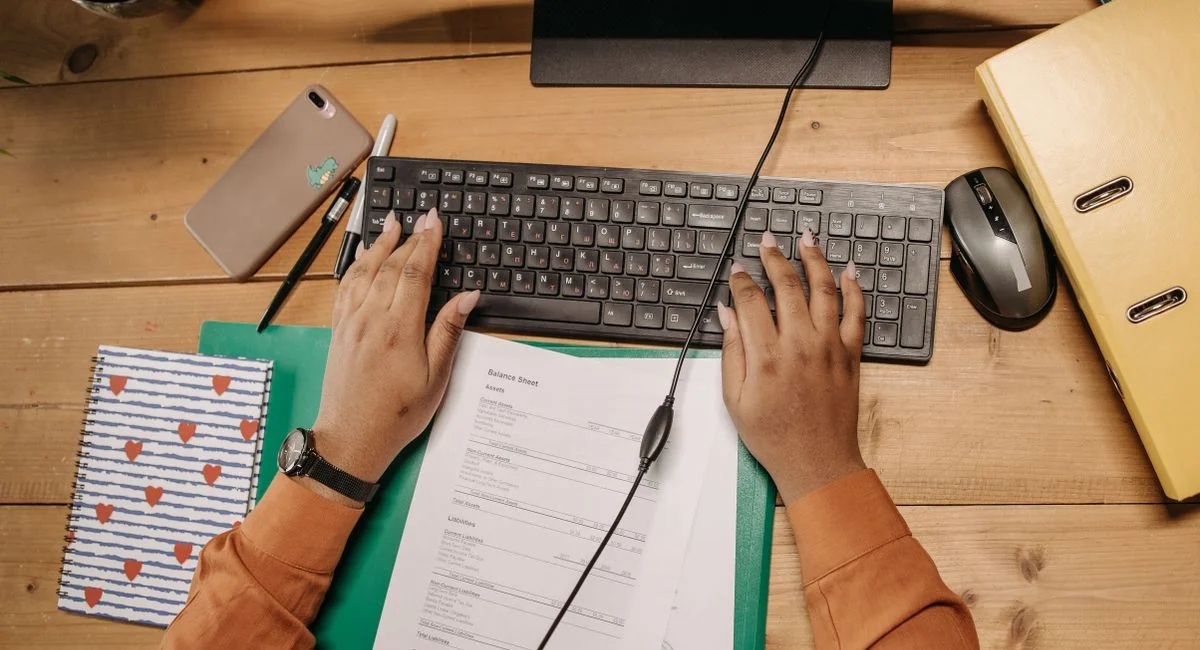 A tidy workspace featuring a keyboard, papers, and office supplies on a wooden desk.