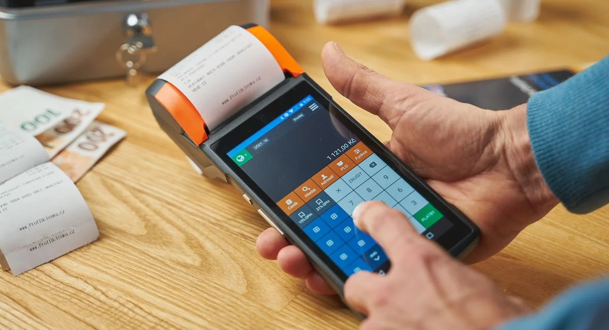 Close-up of hands operating a modern point of sale device with a printed receipt.