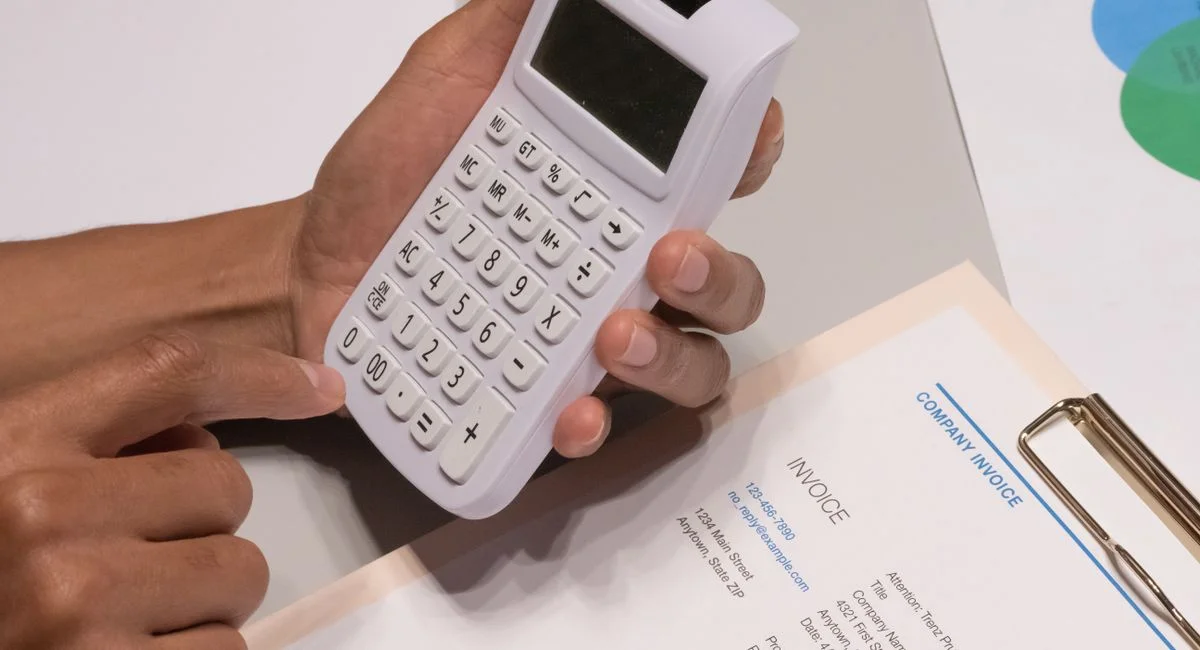 Close-up of hands using a calculator next to a company invoice, depicting a financial calculation concept.