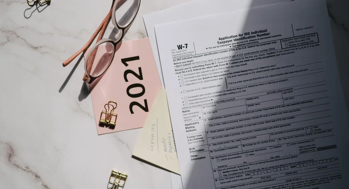 Flat lay of IRS tax documents with reading glasses and 2021 note on a marble surface.
