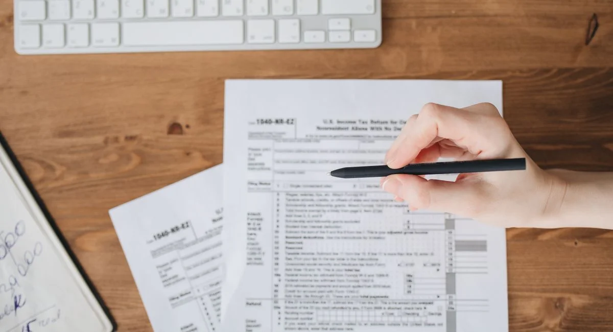Close-up of a hand holding a pen over US tax forms on a wooden table.