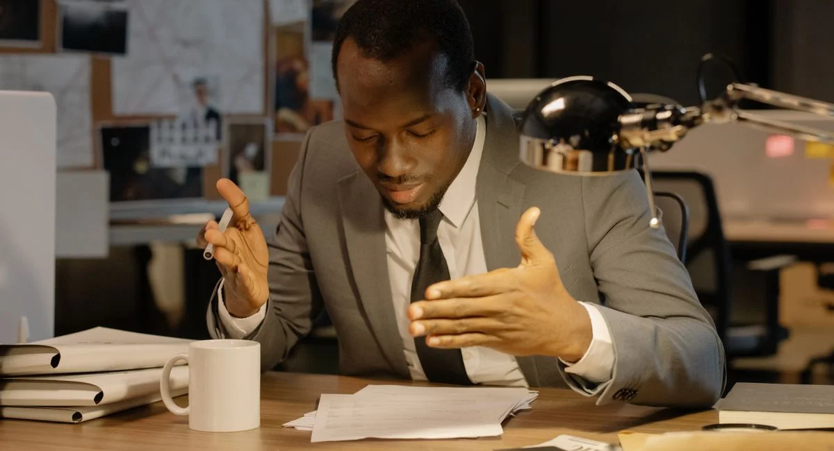 African American man in a gray suit reviewing papers at an office desk.