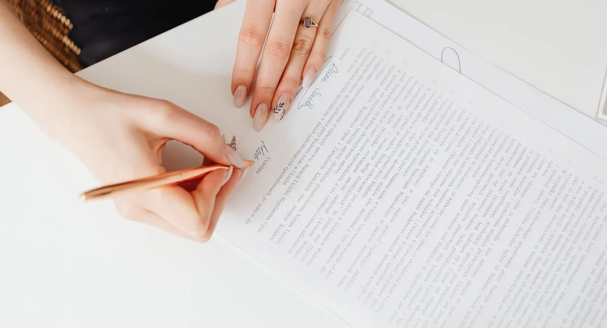 Close-up of woman's hands signing a legal document with elegant nail art using a pen.