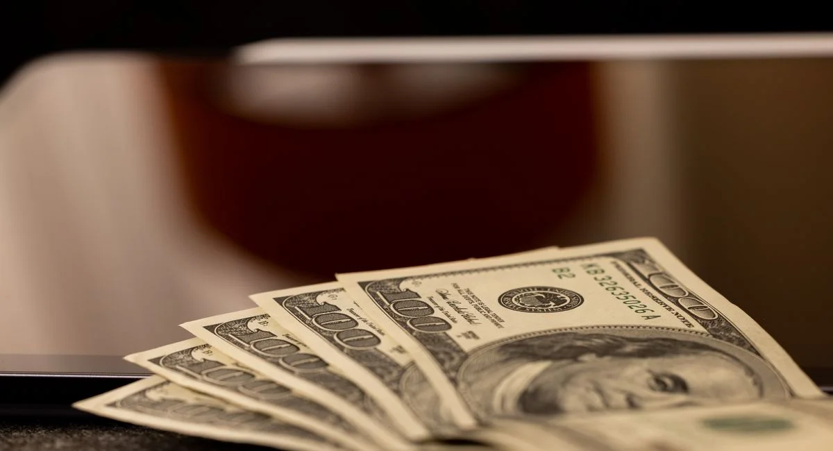 Close-up image of multiple dollar bills placed beside a laptop, symbolizing finance and digital economy.