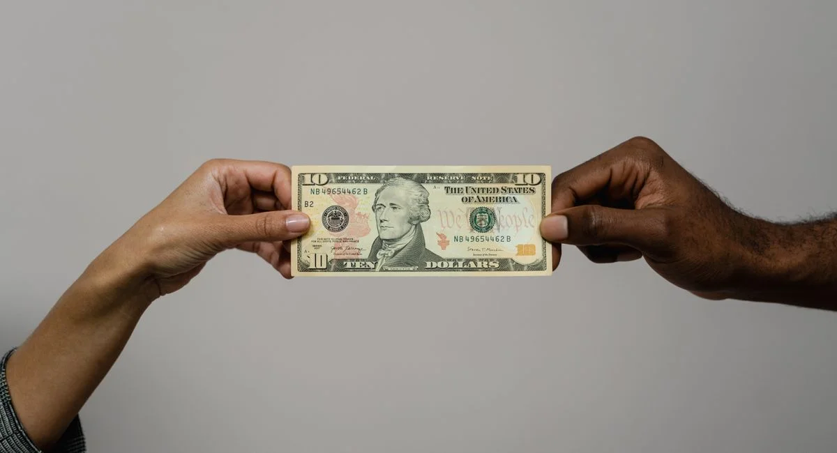 Close-up of two hands exchanging a ten dollar bill, symbolizing financial transaction or exchange.