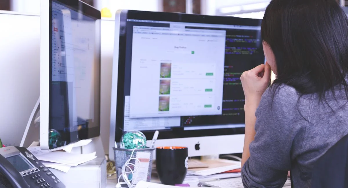 Professional woman focused on work using dual monitors in a modern office.
