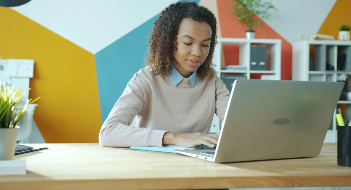 Young woman focused on work at a modern office, using laptop. Bright and vibrant setting.
